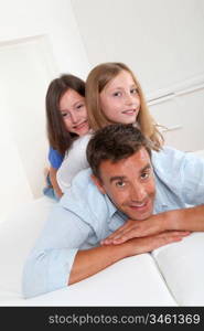 Man lying down on sofa with girls on his back