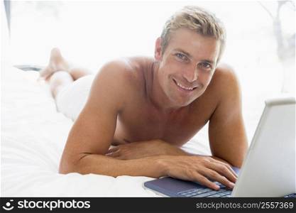 Man lying in bed with laptop smiling
