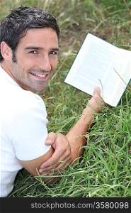 Man lying in the grass reading a book