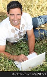 Man lying in the grass using a small laptop computer