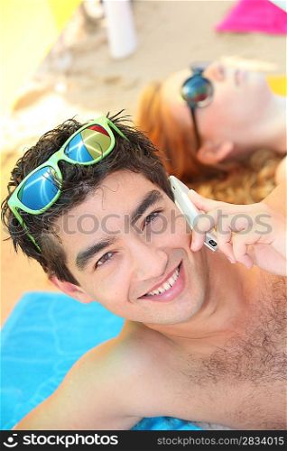 man lying on a beach, using his phone