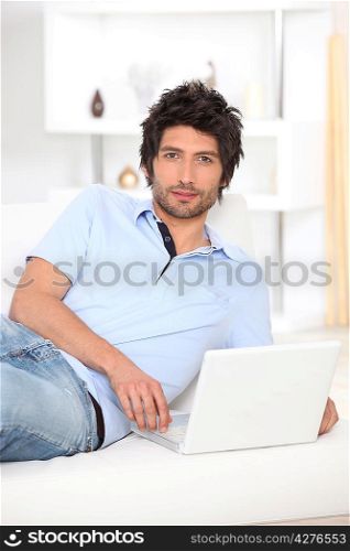 Man lying on a bed and looking at his laptop