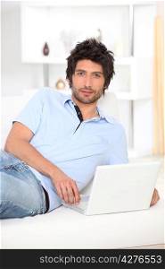 Man lying on a bed and looking at his laptop