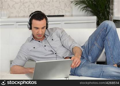 Man lying on a sofa with his laptop and a pair of headphones