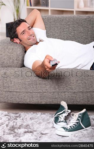 Man lying on couch at home watching television