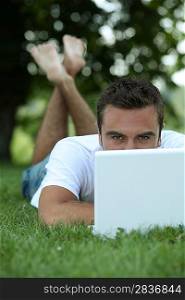Man lying on grass in front of laptop computer
