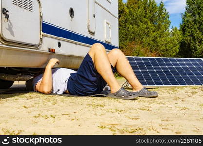 Man lying on ground, repairing bottom of the caravan vehicle.. Man repairing bottom of the rv caravan