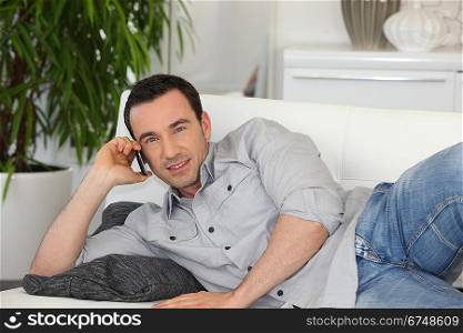 Man lying on his couch and talking on his mobile phone