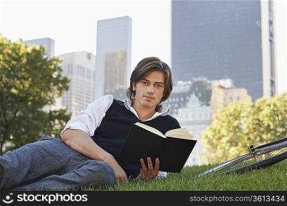 Man lying on lawn, holding book, portrait