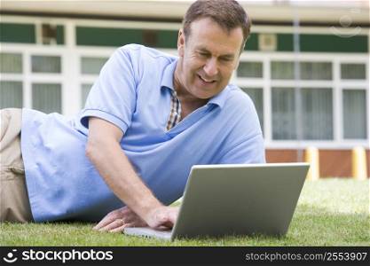 Man lying on lawn of school using laptop