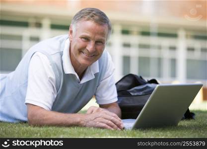 Man lying on lawn of school with laptop