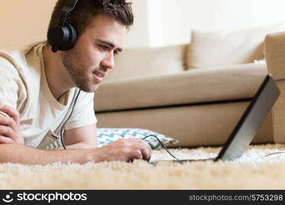 Man lying on the floor using headphones on laptop