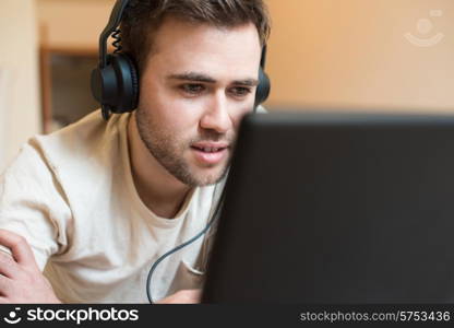 Man lying on the floor using headphones on laptop