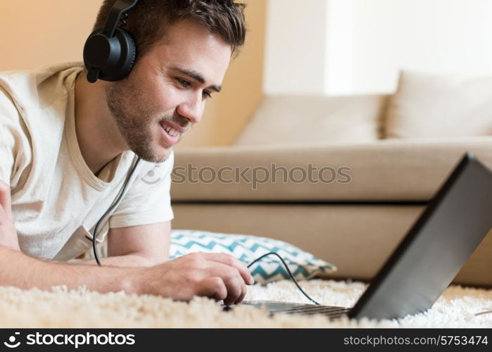 Man lying on the floor using headphones on laptop