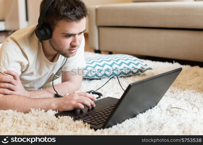 Man lying on the floor using headphones on laptop