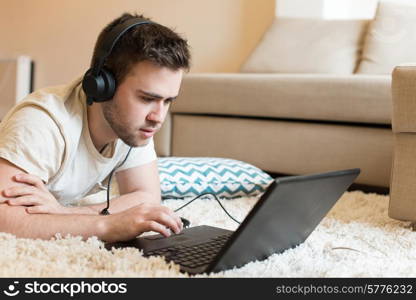 Man lying on the floor using headphones on laptop