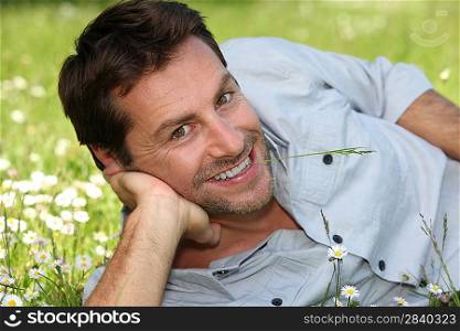 Man lying on the grass and looking at us with a blade of grass in his mouth.