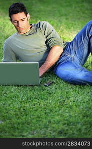 Man lying on the grass in front of laptop