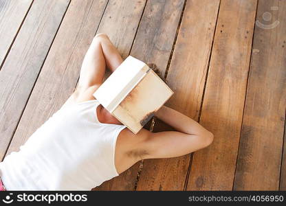 Man lying on wooden floorboards with book over his face