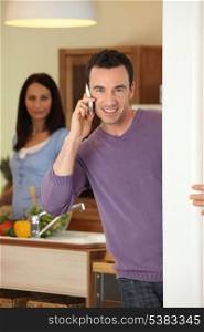 Man making a call whilst wife prepares meal