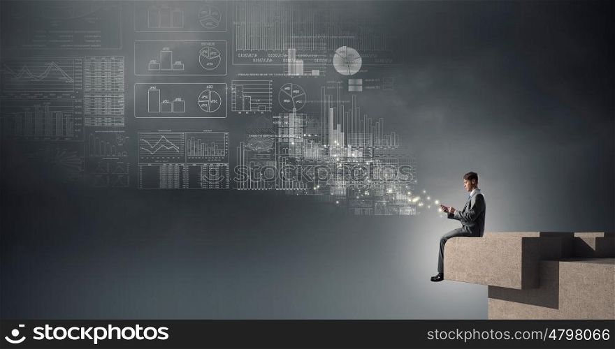 Man making calls with his mobile. Young businessman sitting on building top and using mobile phone