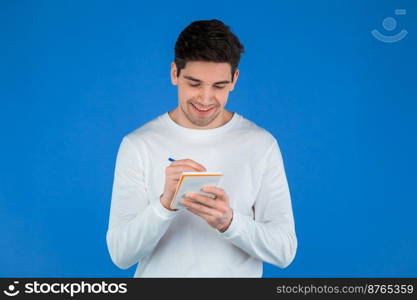 Man making notes in planner, caucasian guy holding pen. He writes future plans and to-do list in notebook for week or month. Keeping personal diary on blue studio background. High quality photo. Man making notes in planner, caucasian guy holding pen. He writes future plans and to-do list in notebook for week or month. Keeping personal diary on blue studio background.