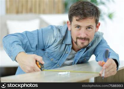 man measuring a wooden board with a tape measure