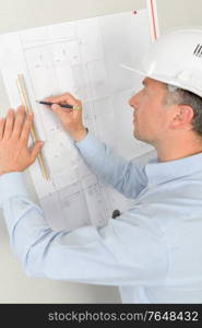 Man measuring plans pinned to wall