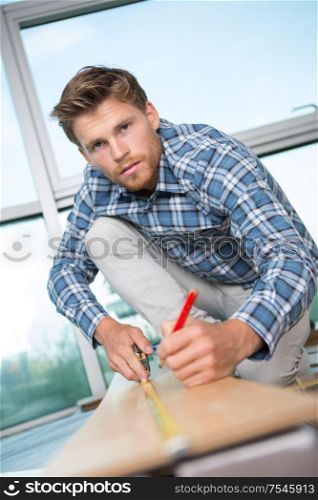 man measuring wooden planks with tape and pencil