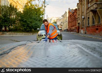 Man mechanic road worker preparing towing truck platform for car loading. Man preparing towing truck for car loading