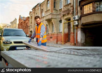 Man mechanic road worker preparing towing truck platform for car loading. Man preparing towing truck for car loading