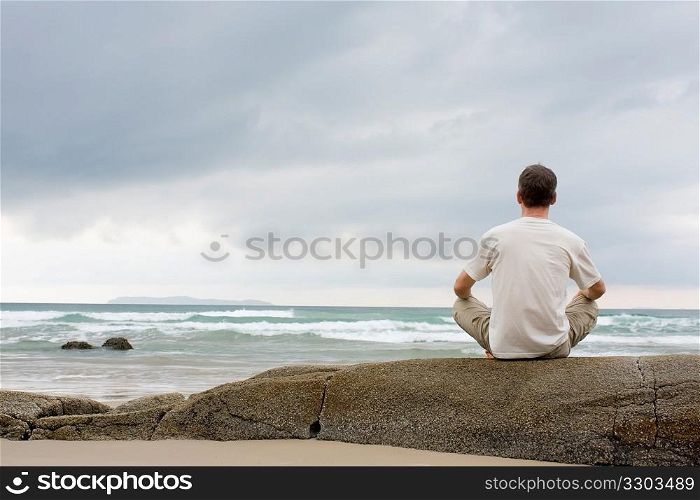 Man meditating on a rock at the sea