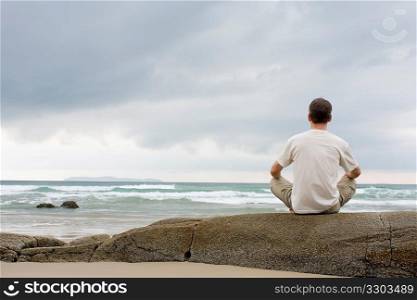 Man meditating on a rock at the sea