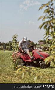 Man mowing his lawn using riding lawnmower. Man maintaining grass in his garden beside house. Man mowing his lawn using riding lawnmower