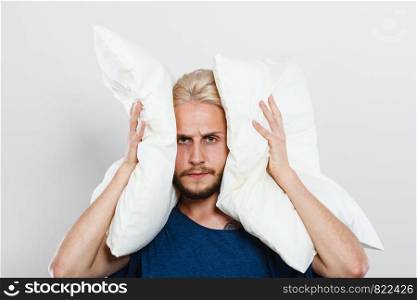 Man need silence. Sad tired young male closing ears with pillows, protecting from loud noise, have head pain. Guy not wanting to listen or can not sleep. Sad man closing ears with pillows