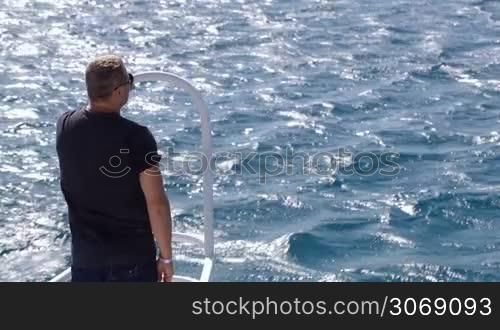Man of 50 years old standing on the bow of sailing yacht and observing clear blue sea