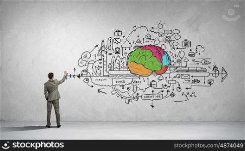 Man of great mind. Back view of businessman drawing human brain on wall