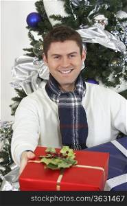 Man offering present in front of Christmas tree