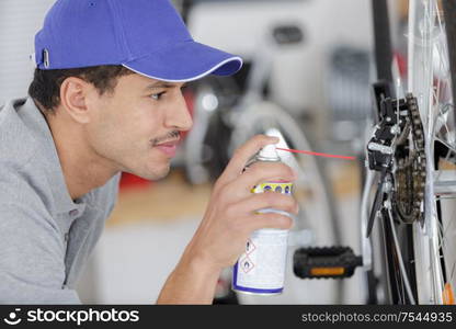 man oiling a bicycle chain and gear with oil spray