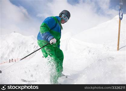 Man on a ski track going downhill, stopping in front of camera dusting some snow