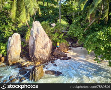 Man on beautiful beach with palm tree and rocks aerial top view drone shot at Seychelles, Mahe