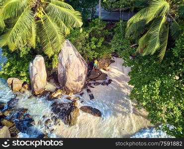 Man on beautiful beach with palm tree and rocks aerial top view drone shot at Seychelles, Mahe