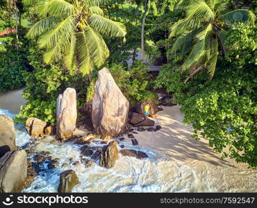 Man on beautiful beach with palm tree and rocks aerial top view drone shot at Seychelles, Mahe