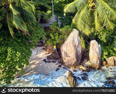 Man on beautiful beach with palm tree and rocks aerial top view drone shot at Seychelles, Mahe