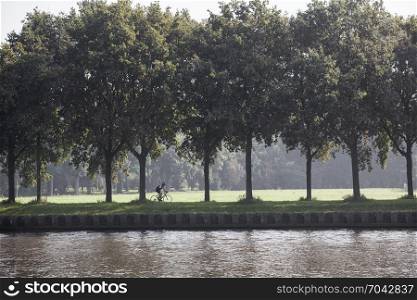 man on bicycle rides along amsterdam rijn canal in holland between Amsterdam and Utrecht on sunny summer day