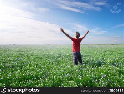 Man on green and blossom meadow of flax reach to sun in deep blue sky. Conceptual scene.