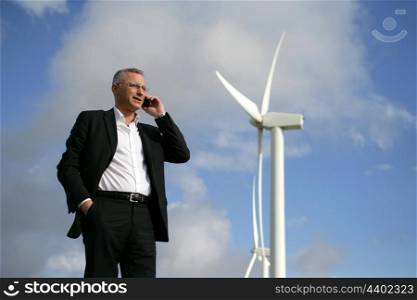 Man on mobile phone next to wind turbine