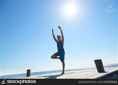 Man on pier standing on one leg arms raised exercising
