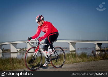 Man on road bike riding down open country road, bridge on background.