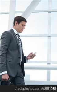Man on smart phone - young business man in airport. Businessman using smartphone inside office building or airport.